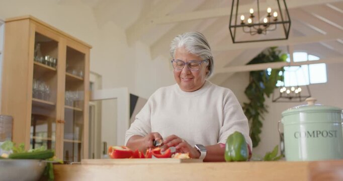 Senior African American woman chopping halved red pepper on cutting board at counter prepping meal