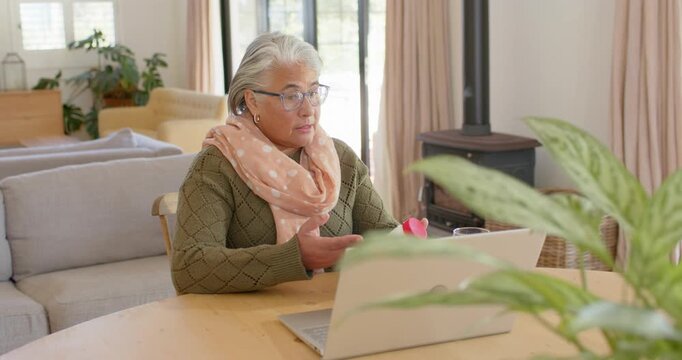 Senior African American woman in green sweater at wooden table showing container to laptop on call