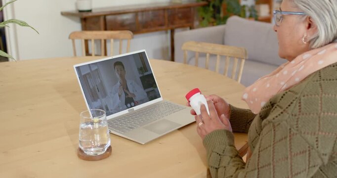 Senior African American woman checking red-cap bottle via laptop call verifying dosage, copy space