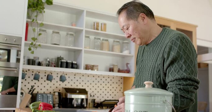 Mature Asian man placing knife, slicing carrots at wooden counter for meal prep, compost