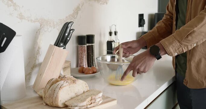 African American man cracking eggs into glass bowl at counter, whisking for breakfast, copy space