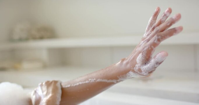 African American woman raising right arm in bathtub, soaping and washing forearm to cleanse skin