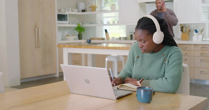 Couple man speaking on phone pacing to kitchen table while woman working on laptop with headphones