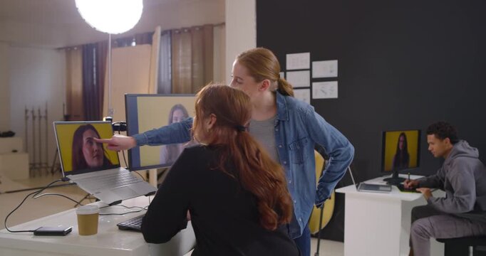 Two adult women leaning in, pointing at portrait on monitor, reviewing for retouch and selection