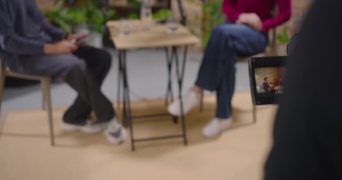 Two hosts speaking, gesturing at mics on set, camera operator adjusting framing to record interview