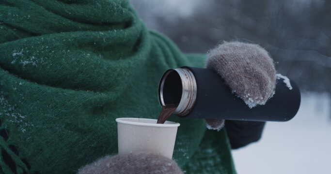 teenage girl pouring hot cocoa into paper cup in park on a winter day