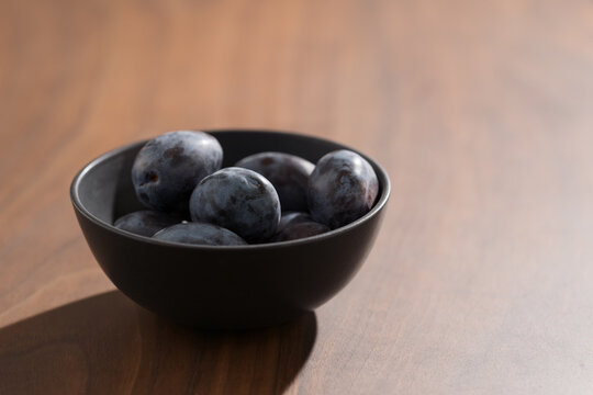 Bowl of fresh plum on walnut wood table with copy space