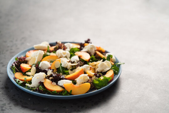 salad with nectarines, mozzarella and mixed greens in blue plate on concrete background with copy space