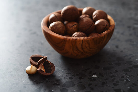 Inshell macadamia nuts in olive wood bowl on terrazzo surface
