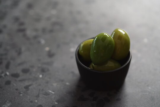 big green olives in black bowl on concrete background