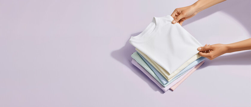 Hands Holding Stack of Neatly Folded Shirts on Pastel Background, Wide Banner for Laundry Care, Detergent and Household Cleaning Advertising with Copy Space