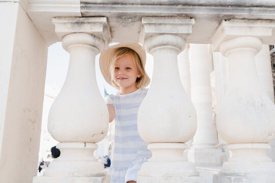 Cute little girl playing peekaboo between white stone pillars