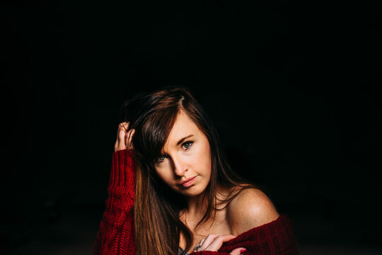 A young woman in a red sweater looks directly at the camera