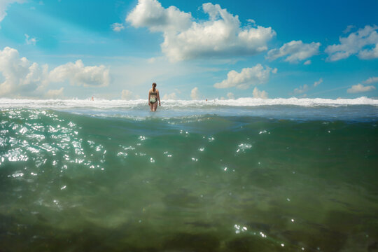 Woman in bikini wading into the ocean surf on a sunny day
