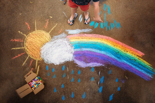 A child draws a colorful chalk rainbow on the pavement
