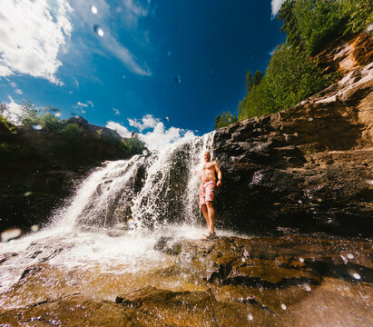 Man stands on rocks next to a cascading waterfall