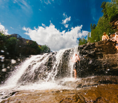 Young man cools off under a rushing waterfall on a sunny day