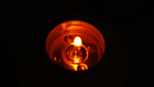 Concentric rings of reflected candle light glowing around a blurred flame in the metal cup of a tea light, hypnotic circular pattern on black, concept of meditation focus, trance and inner calm