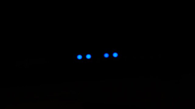 Four blue status lights blinking in a dark server room, sharp glowing LED indicators of network hardware in total darkness, concept of data center operations, cloud computing and nonstop digital infr