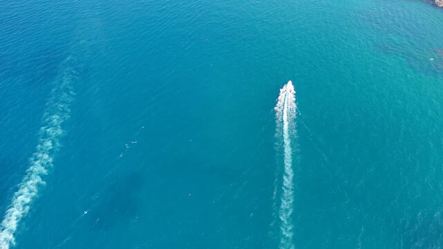 Top down aerial view of two speedboats racing in parallel across bright turquoise water, long white wakes trailing behind them off the Polignano a Mare coast, concept of summer speed and boat excursi