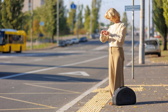 Mature Woman Checking Time Waiting for Bus with Suitcase at City Bus Stop