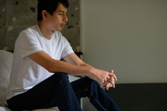 Thoughtful Young Man Sitting on Bed in Minimalistic Room