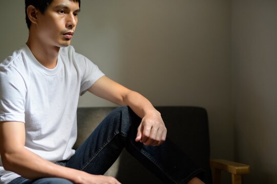 Thoughtful young man sitting on a sofa with pensive expression