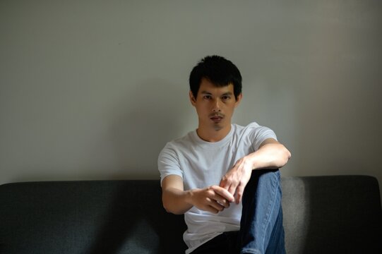 Young Man Sitting on Couch in Casual Attire with Thoughtful Expression