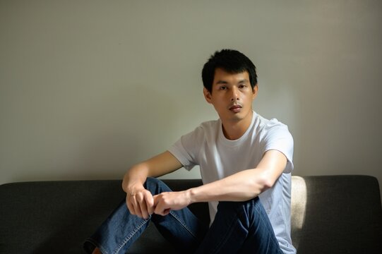 Thoughtful young man sitting on a couch in soft light