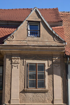 An ornate historicist building facade featuring a classic wooden window framed by pilasters under a large triangular roof dormer.