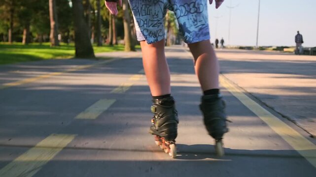 Feet shift through alternating inline skating strides over yellow lane markings. Low rear close-up isolates moving boots, coordinated weight transfer. Balance, outdoor exercise, recreational footwork.