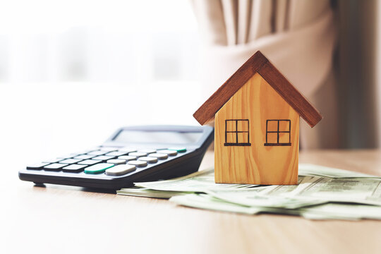 A wooden house model placed on a stack of banknotes and a calculator on a table. concepts of real estate investment, home loans.