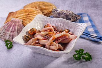 Fresh seafood mix with squid and mussels in white bowl surrounded by seashells and parsley © Andrei Starostin