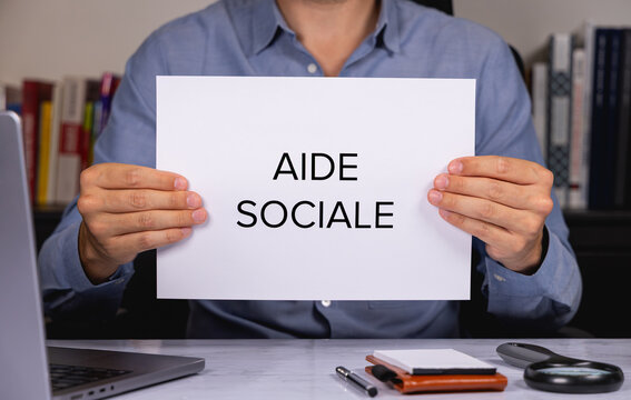 Une personne en chemise tenant une feuille de papier sur laquelle est &eacute;crit en gros les mots aide sociale.