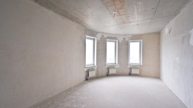 Sparse room in pre‑finish stage. three windows with white frames, radiators below, rough plaster walls, and exposed ceiling edges