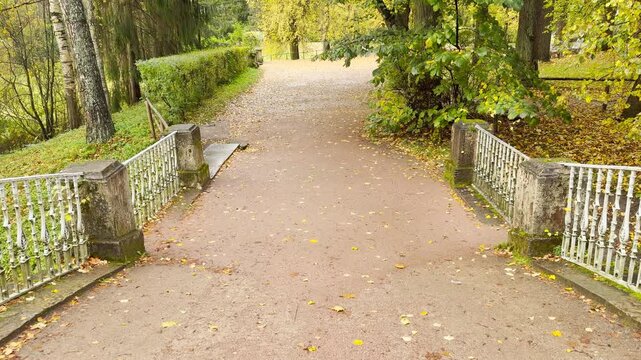 POV walkthrough of an empty bridge path, shot on stabilizer in Pavlovsk Park, Russia, slow motion. Smooth forward camera motion creates a serene, quiet, and melancholic rainy autumn mood.
