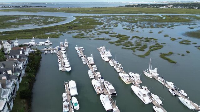 Organized rows of yachts fill Mount Pleasant Basin berths bordering sprawling salt flats along Mount Pleasant Waterways. Nautical vessels gleam under overcast skies reflecting onto calm sea, SC