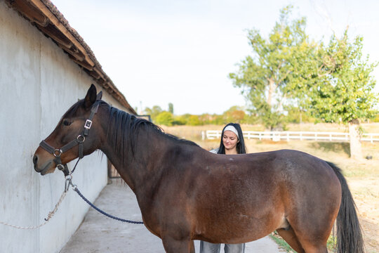A young, dark haired woman prepares her horse for a ride at dusk on an autumn day. She grooms him, kisses him, and whispers to him, showing him how much she loves him.