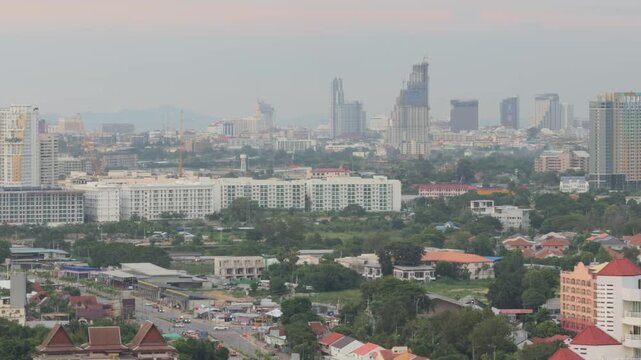Aerial view of Pattaya cityscape with modern skyscrapers and green trees at sunset, Thailand. Cinematic drone shot of urban architecture, tropical city streets and cloudy sky in evening light.