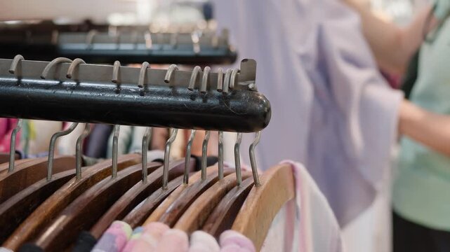 Close-up of wooden hangers on a rack as a woman browses and chooses light clothing in a fashion store or boutique. Retail trade, consumerism, apparel shopping and customer service concept.