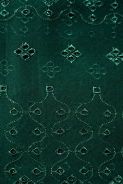 Dark green fabric with intricate embroidery and cutwork patterns for