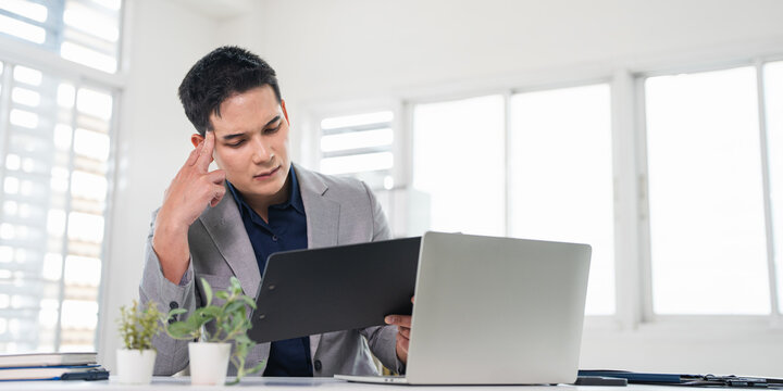A stressed businessman experiences financial crisis, bank debt. Man sitting at desk holding receipt or financial report feels desperate .