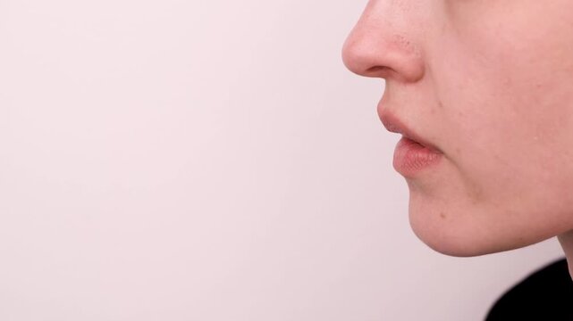 A person is blowing air from their mouth while standing near a wall. This action takes place in a basic indoor area with a neutral background.