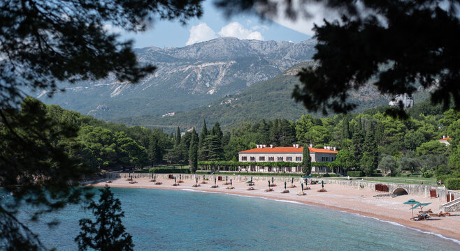 Scenic view of the historic Villa Milocer and King's Beach in Montenegro, framed by green pine branches