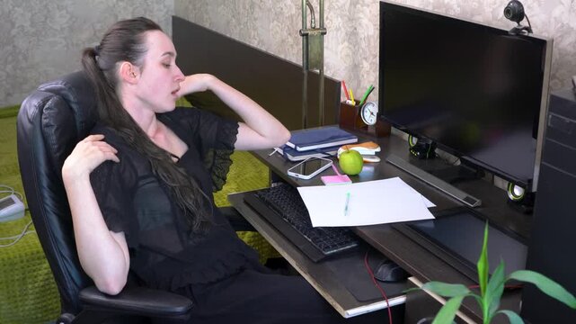 A person is sitting at a desk in a home office while looking overwhelmed. Papers and a green apple are on the desk. A monitor shows the person is focused on work tasks.