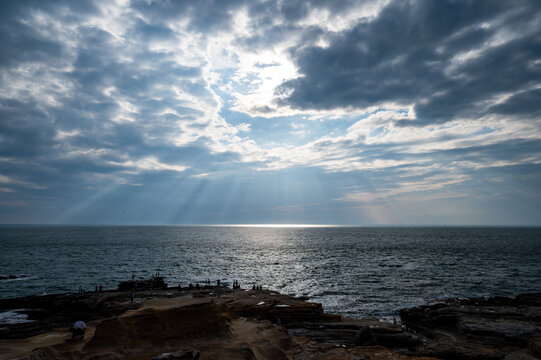 雲の隙間から海へと差し込む神秘的な光線（薄明光線・天使の梯子）と岩切立つ海岸風景