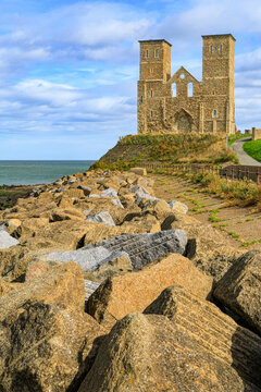 The medieval twin spires of Reculver Towers perched on a clifftop above a massive rock riprap coastal defense barrier, Reculver, Kent, England