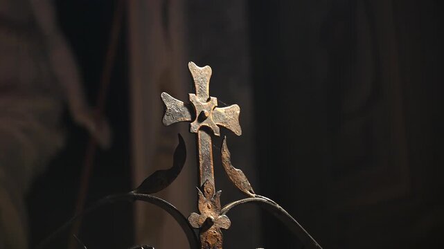 Decorative iron cross remains still atop curved wrought iron scrolls. Antique religious craftsmanship catches warm light in dim interior, lending metal ornament reverent. Creed and religion concept