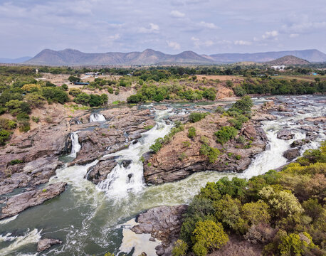 Aerial view of the Kaveri river forming rapid streams and cascading waterfalls over rocky terrain in the picturesque landscape of Western ghats, India.