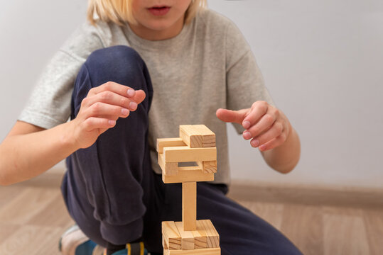 Young child concentrating on building a wooden block tower at home, developing fine motor skills, creativity and problem solving through constructive play and focused learning